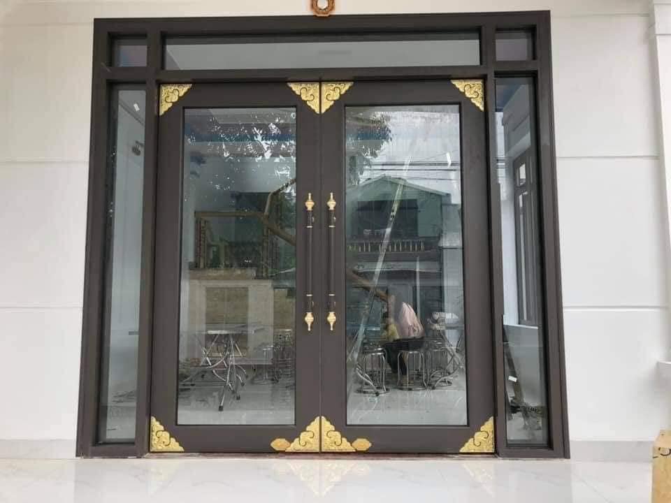 Cửa nhôm kính hai cánh màu nâu có hoa văn inox mạ vàng sang trọng cho mặt tiền nhà
