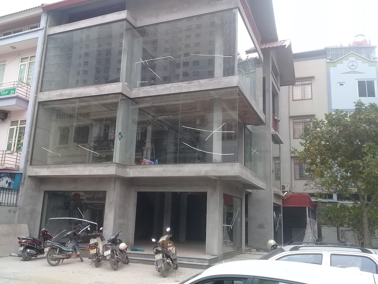 Tòa nhà đang xây dựng với mặt tiền kính lớn và nhiều xe máy đỗ phía trước