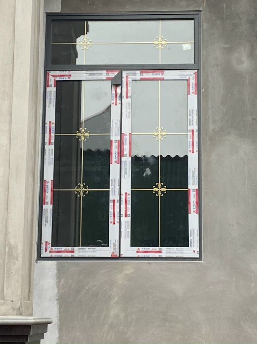 Cửa sổ nhôm kính hai cánh màu xám, khung trắng viền đỏ, nan hoa đồng trang trí trên nền tường xi măng