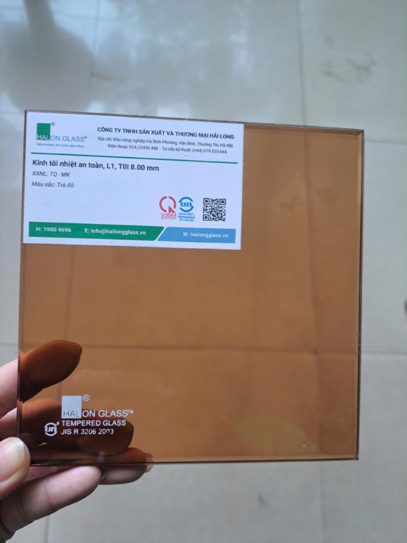 Tấm kính cường lực màu trà đỏ HALON GLASS dày 8mm cầm trên tay, tem nhãn sản phẩm tiếng Việt