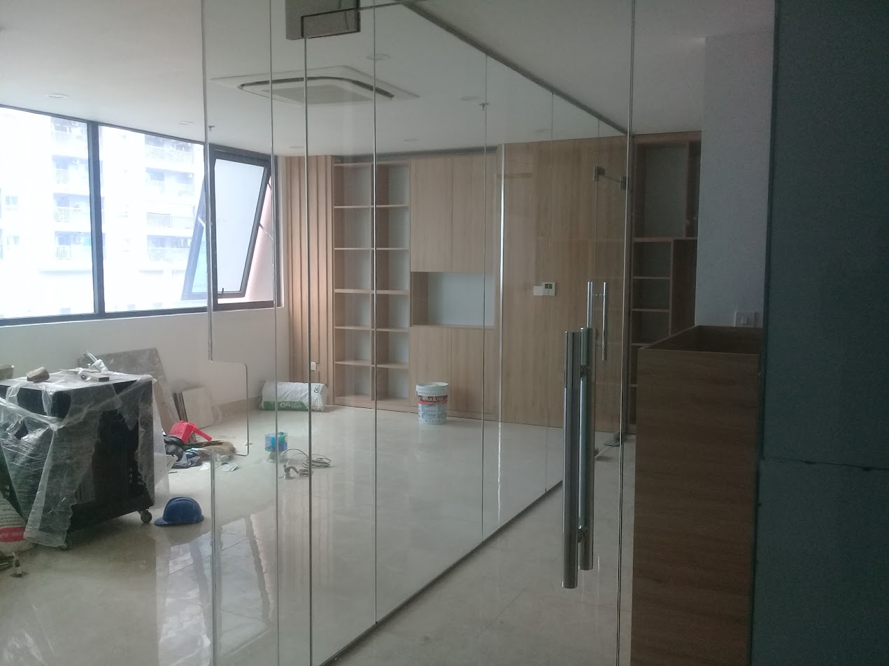 Vách kính cường lực ngăn phòng làm việc đang thi công với cửa kính tay nắm inox và tủ gỗ âm tường