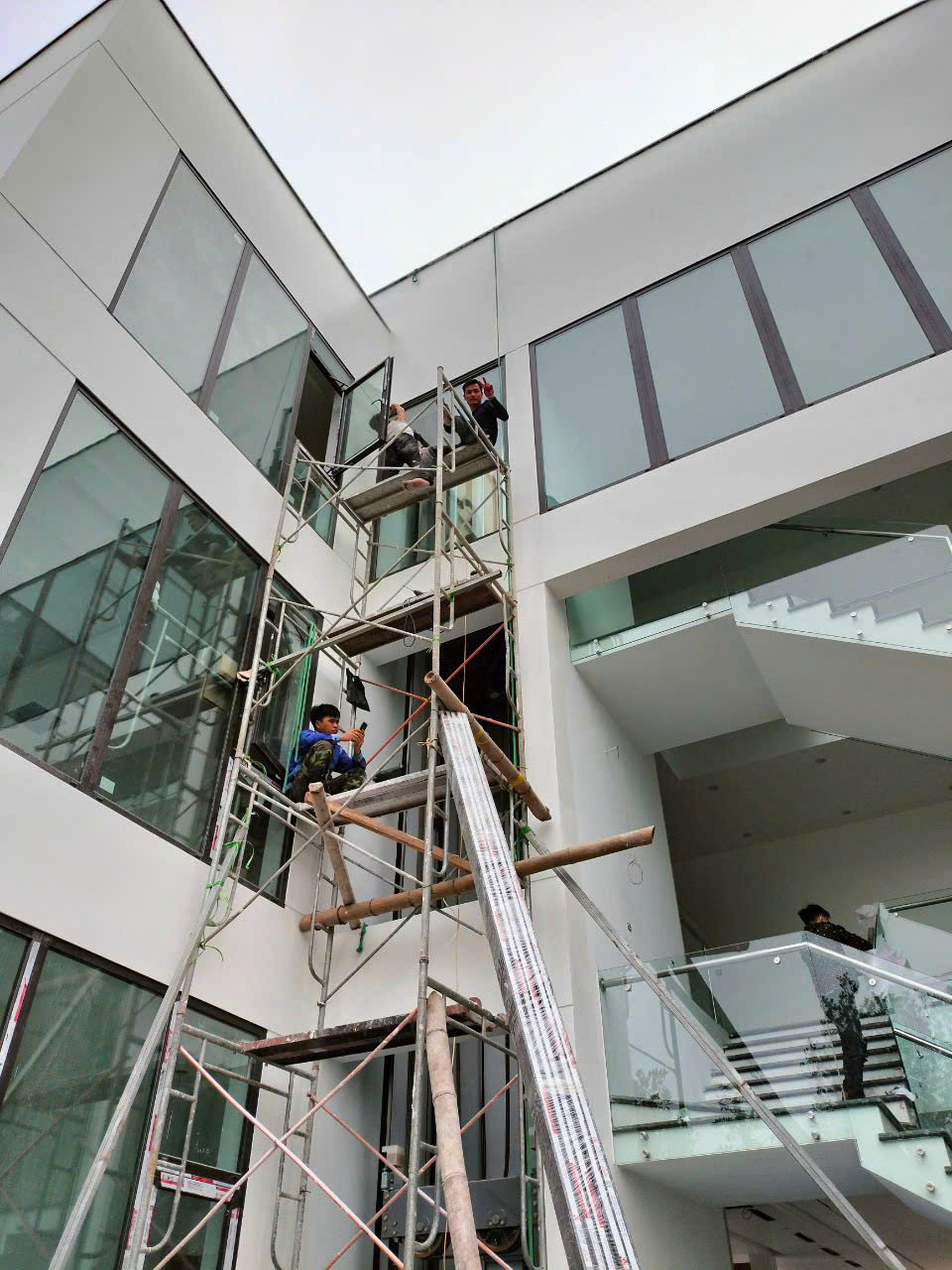 Công nhân lắp đặt kính mặt dựng cho nhà phố hiện đại bằng giàn giáo cao